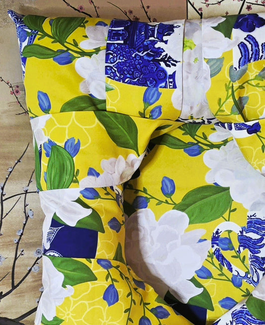 A close-up of an overstuffed picture frame with a chinoiserie and floral print. The design features a bright yellow background with white flowers, green leaves, blue tulips, and blue-and-white porcelain-style patterned teacups.