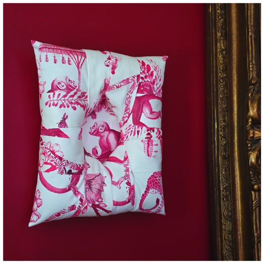 An overstuffed picture frame with a pink and white toile de Jouy monkey pattern, displayed against a dark red background with an ornate gold picture frame visible at the side.