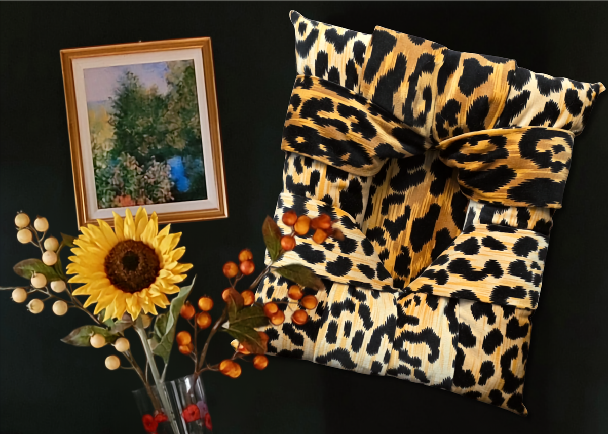 A velvet leopard-print fabric picture frame displayed on a dark background next to a sunflower, berries, and a framed landscape painting.