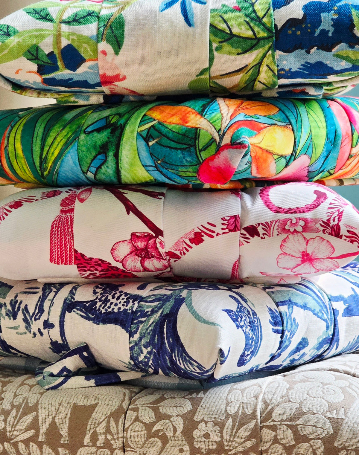 A stack of folded patterned overstuffed picture frames showing multiple tropical and floral designs in green, blue, pink, orange, and red on white backgrounds.